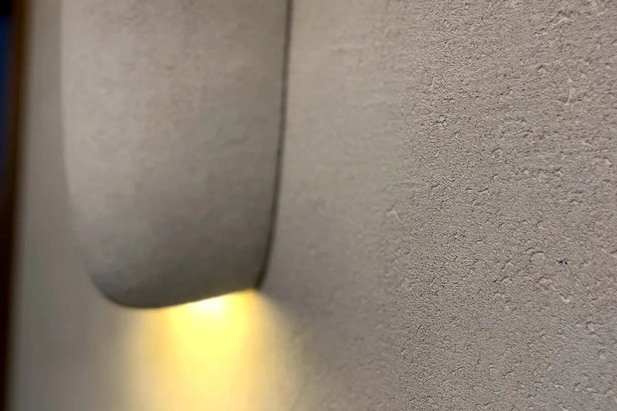Aplique de pared encendido sobre revestimiento de cal, luz rasante que revela la textura