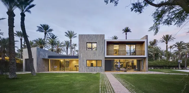 Fachada de la vivienda unifamiliar rodeada de palmeras al atardecer